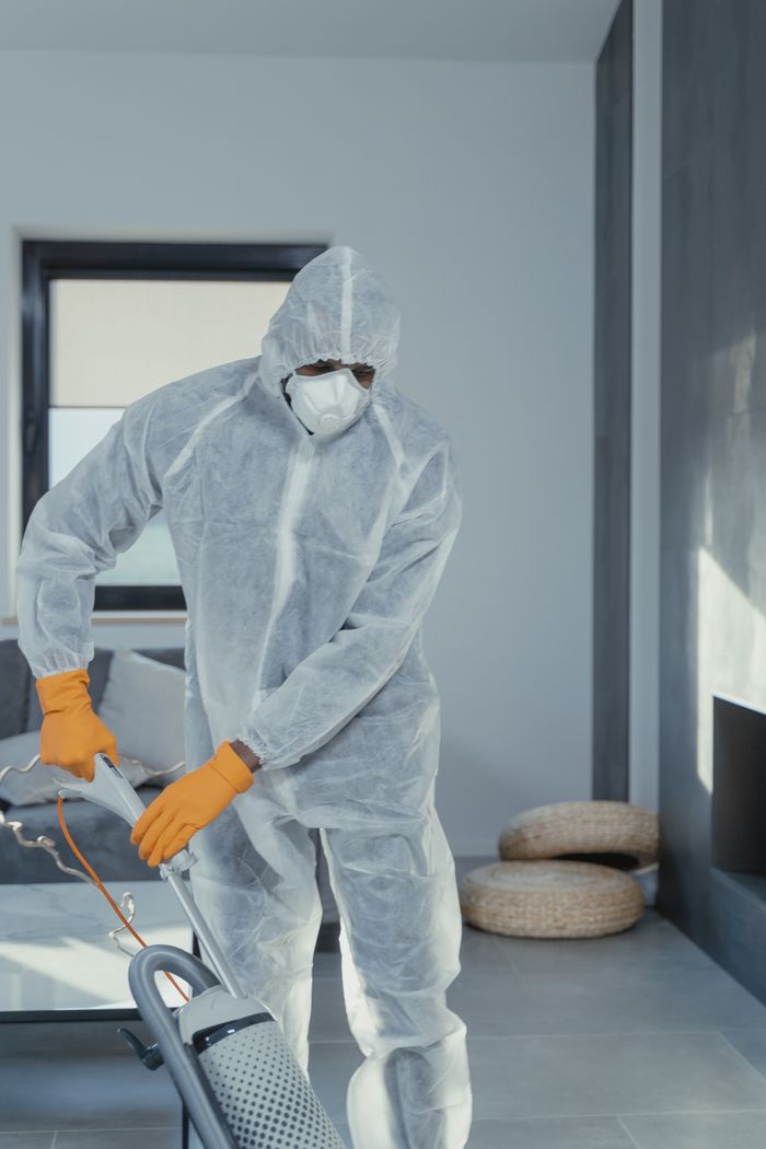 gallery-04 A person in personal protective equipment vacuuming indoors, ensuring a thorough clean.