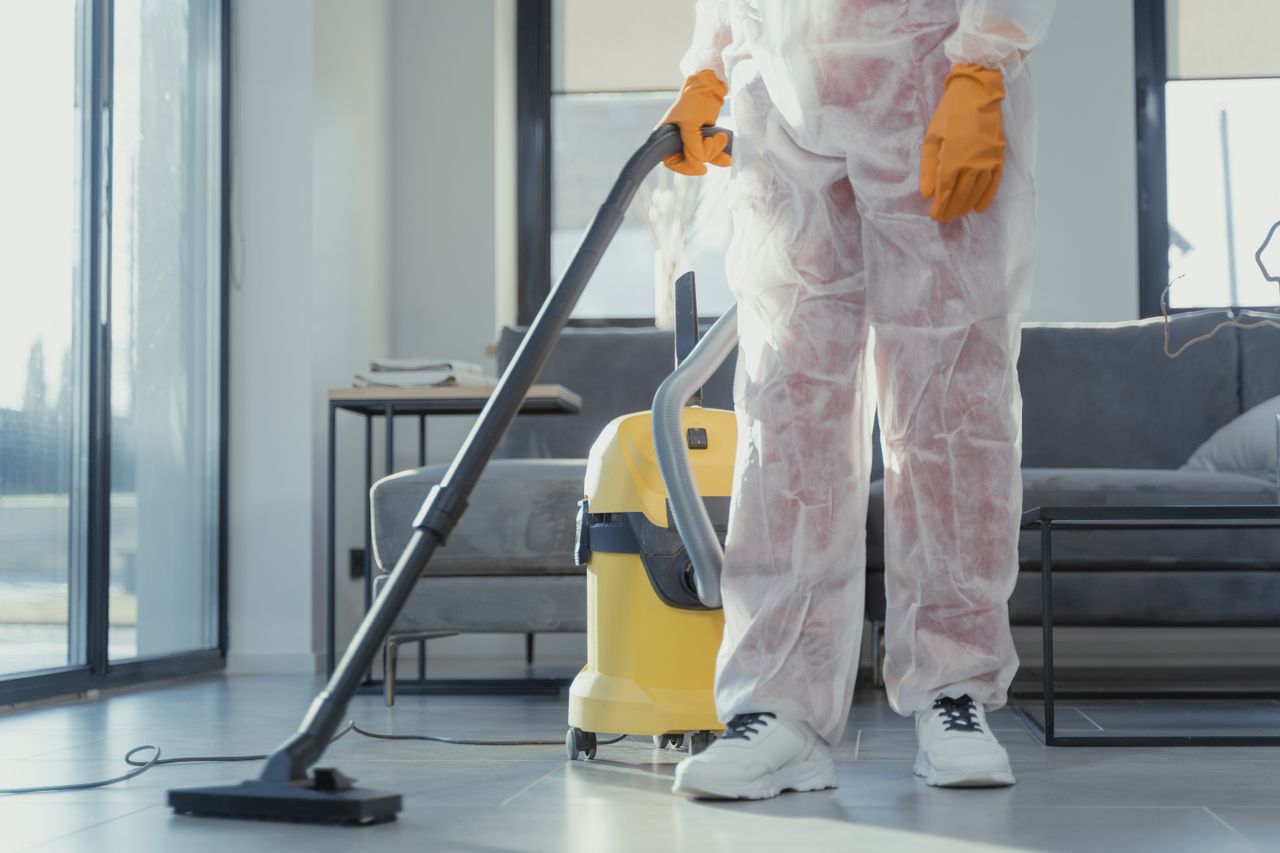 about-img-01 A cleaner in protective coveralls and gloves vacuuming a modern living room.